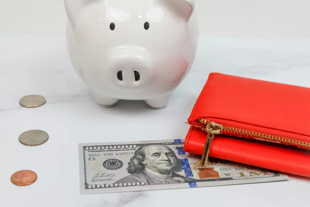 White piggy bank with coins, a dollar bill and a red wallet